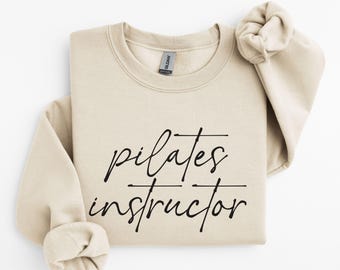 May include: A beige sweatshirt with the text "pilates instructor" written in black cursive.
