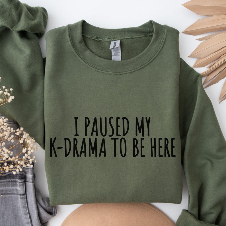 May include: A green sweatshirt with the text "I paused my K-drama to be here" printed in black.