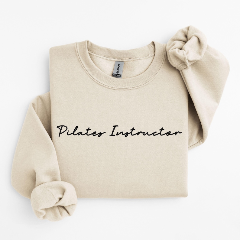 May include: A beige sweatshirt with the text "Pilates Instructor" in black cursive writing.