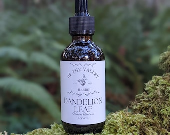 May include: A dark brown glass bottle with a black dropper top. The bottle is labelled "Of The Valley" with a small flower design and the text "Est. 2020 Herbs Dandelion Leaf Herbal Tincture 2 Ounces".
