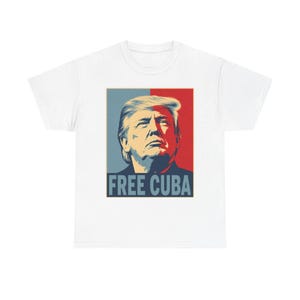 May include: A white short-sleeved t-shirt featuring a graphic print of Donald Trump. The design uses a split blue and red background with the text FREE CUBA printed in bold blue capital letters at the bottom of the rectangular portrait graphic.