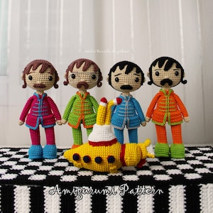 May include: Four crocheted dolls with brown or black hair and mustaches, wearing colorful jackets and pants in pink, green, blue, and orange. A yellow crocheted submarine with dark blue portholes sits in front. Text reads Amigurumi Pattern.