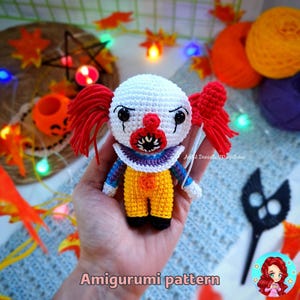 Pode incluir: Padrão de amigurumi para um palhaço de crochê com cabelo vermelho, pele branca, nariz vermelho e um sorriso cheio de dentes. A boneca está vestindo uma roupa amarela e azul com uma gola roxa.
