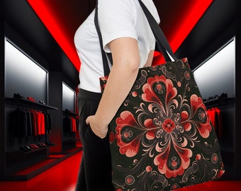Op de afbeelding: Een zwarte tote bag met een rood en wit bloemenpatroon. De tas heeft een lange band en wordt door een persoon gedragen.