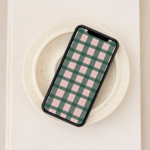 May include: A black smartphone with a pink and green plaid pattern on the screen. The phone is lying on a white plate.