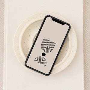 Puede incluir: Un teléfono inteligente negro con un fondo beige y un diseño geométrico simple de arcos negros y un círculo en la pantalla.