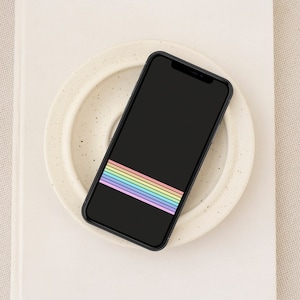 Puede incluir: Un teléfono inteligente negro con un fondo de pantalla de rayas arcoíris en un plato blanco moteado.