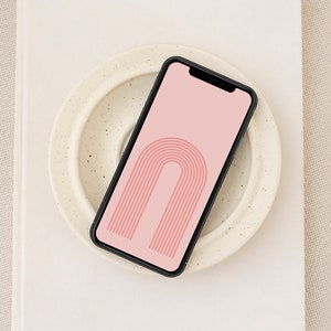 Puede incluir: Un teléfono inteligente negro con un fondo rosa y un diseño de arco con rayas rojas y blancas.