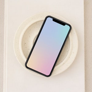 May include: A black smartphone with a gradient screen from pink to blue, resting on a white ceramic plate with a speckled pattern.