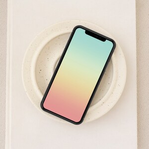 Op de afbeelding: Een zwarte smartphone met een gradiëntscherm dat een roze, gele en groene kleurschakering weergeeft. De telefoon ligt op een wit keramiek bord met een gespikkeld patroon.