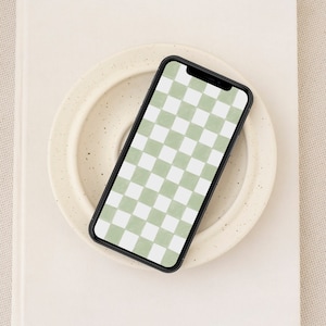Puede incluir: Un teléfono inteligente negro con un patrón de cuadros verde y blanco en la pantalla, descansando sobre un plato de cerámica blanco.