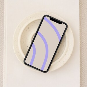 May include: A black smartphone with a light beige background and two purple curved lines on the screen.