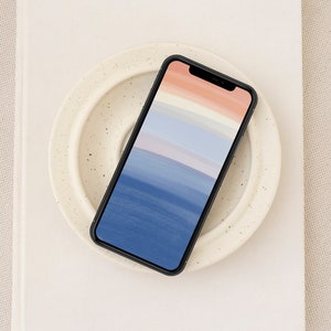 Puede incluir: Un teléfono inteligente negro con un fondo abstracto azul y rosa sobre un plato blanco moteado.