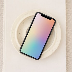 May include: A black smartphone with a gradient rainbow screen is on a white ceramic plate with a speckled pattern.