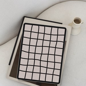 May include: A black and white grid pattern on a light pink background. The grid pattern is on a piece of paper that is folded in half and placed on a white surface.