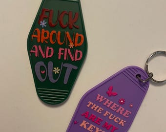 Può includere: Due portachiavi a forma di chiavi di camera d'albergo. Il portachiavi verde dice "F*ck Around and Find Out" con lettere rosa, rosse e arancioni e fiori. Il portachiavi viola dice "Where the f*ck are my keys" con lettere rosa, rosse e arancioni e fiori.