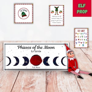 Puede incluir: Un duende rojo y blanco con un gorro rojo y una barba blanca. El duende sostiene un cartel que dice "Fases de la Luna Edición Duende". El cartel tiene una imagen de la luna en diferentes fases. El duende está sentado sobre una superficie de madera.