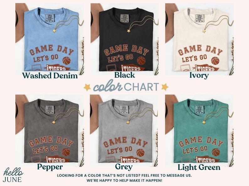 May include: A colour chart shows six t-shirts in different shades: Washed Denim, Black, Ivory, Pepper, Grey, and Light Green. Each shirt has the text "GAME DAY LET'S GO TIGERS" with a basketball graphic. A gold necklace is draped on each shirt.