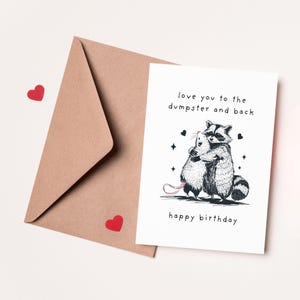 Puede incluir: Una tarjeta de cumplea&ntilde;os con una ilustraci&oacute;n en blanco y negro de un mapache abrazando a una rata. La tarjeta dice "love you to the dumpster and back happy birthday".