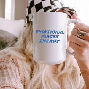 Op de afbeelding: Een witte keramische mok met blauwe tekst die "Emotional Pisces Energy" zegt.