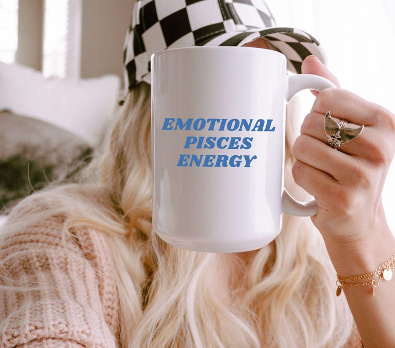Op de afbeelding: Een witte keramische mok met blauwe tekst die "Emotional Pisces Energy" zegt.