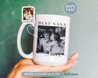 May include: White ceramic mug with a large handle, featuring a black and white photo of a grandmother and grandchild. The mug has the words "BEST NANA ever" printed on it. A small photo is on the upper left corner. The mug is held by a person.