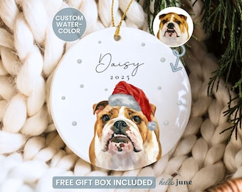 May include: White ceramic Christmas ornament featuring a watercolor illustration of a bulldog wearing a Santa hat. The ornament is personalized with the name "Daisy" and the year "2025". Includes a gold string for hanging.