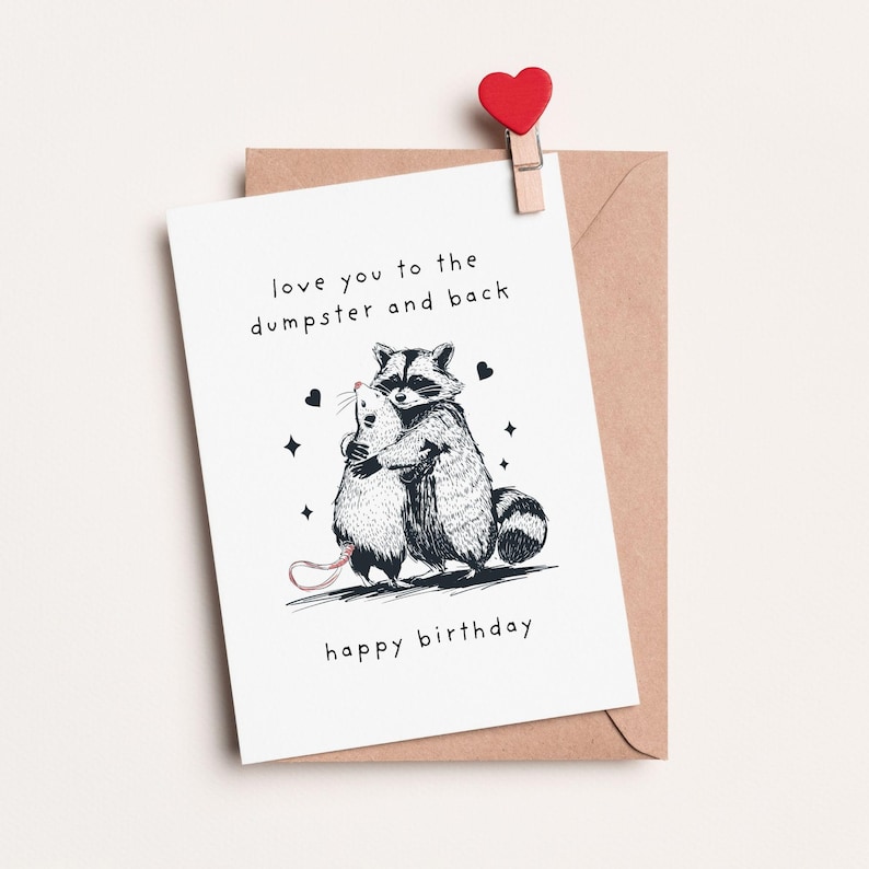 Puede incluir: Una tarjeta blanca con una ilustraci&oacute;n en blanco y negro de un mapache abrazando a una rata. La tarjeta dice "love you to the dumpster and back" y "happy birthday".
