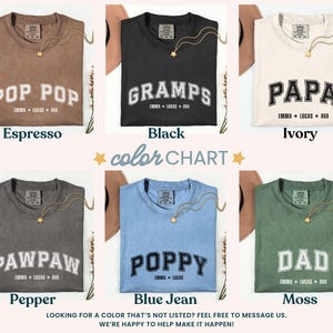 May include: A color chart of six t-shirts in various colors, including espresso, black, ivory, pepper, blue jean, and moss. Each shirt features a different name in a collegiate font, such as "POP POP" and "GRAMPS". A gold necklace with a star pendant is draped on each shirt.
