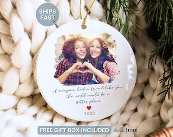 May include: A white ceramic ornament with a gold string, featuring a photo of two smiling people making a heart shape with their hands. Text reads "if everyone had a friend like you the world would be a better place" with a red heart and the year 2025.