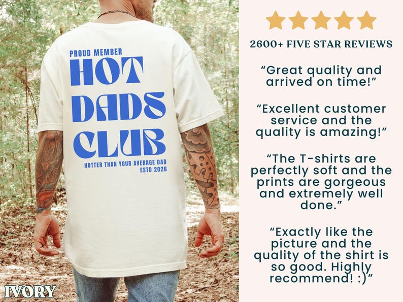 May include: Ivory-colored t-shirt with the text "HOT DADS CLUB" in blue, along with the phrases "PROUD MEMBER" and "HOTTER THAN YOUR AVERAGE DAD ESTD 2026". The shirt has a crew neck and short sleeves.