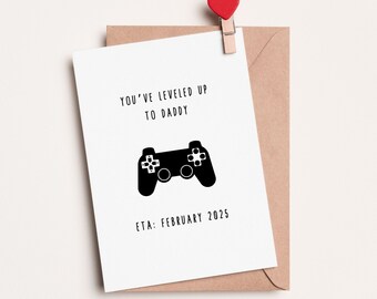 May include: A white card with black text that reads "You've leveled up to Daddy. ETA: February 2025." A black silhouette of a video game controller is in the center of the card.