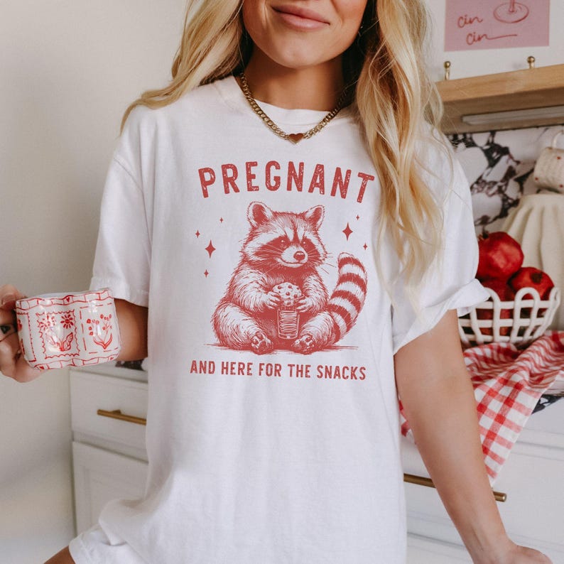 May include: White t-shirt with a red graphic of a raccoon holding a snack and the text "PREGNANT AND HERE FOR THE SNACKS".