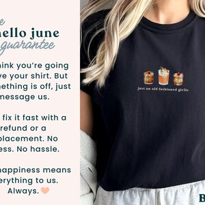 Może przedstawiać: Czarny t-shirt z małą grafiką trzech koktajli i napisem "just an old fashioned girlie". Koszulka ma r&oacute;wnież napis "the hello june guarantee" i słowo "BLACK" na dole.