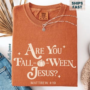 May include: An orange Comfort Colors t-shirt with the text "Are You Fall-Ween Jesus?" and "Matthew 4:19" printed on the front. A silver necklace and a pair of blue jeans are also in the image.