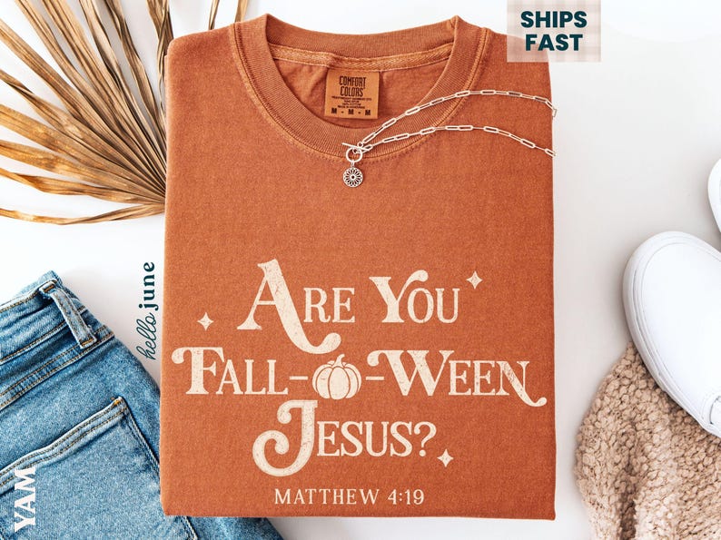 May include: An orange Comfort Colors t-shirt with the text "Are You Fall-Ween Jesus?" and "Matthew 4:19" printed on the front. A silver necklace and a pair of blue jeans are also in the image.