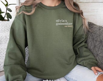 May include: A green sweatshirt with the text "olivia's godmother est 2023" on the front.
