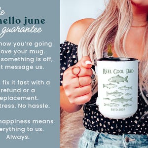 May include: White ceramic mug with a black rim featuring the text "REEL COOL DAD" and illustrations of fish. The mug also has the text "ESTD 2028". The image includes text that says "the hello june guarantee".
