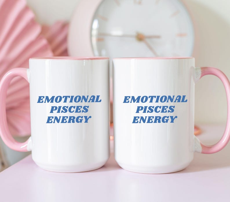 Op de afbeelding: Twee witte keramische mokken met roze randen. Beide mokken hebben de tekst "Emotional Pisces Energy" in blauw op de voorkant.
