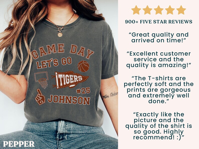 May include: Dark grey t-shirt with a basketball-themed graphic. The design includes the words "GAME DAY LET'S GO TIGERS #25 JOHNSON" in a distressed style. The shirt also features a basketball and a basketball hoop.