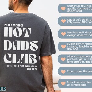 May include: Dark gray unisex t-shirt with the text "PROUD MEMBER HOT DADS CLUB" in white. The shirt also includes the phrase "HOTTER THAN YOUR AVERAGE DAD ESTD 2026". The shirt is made of 100% cotton.