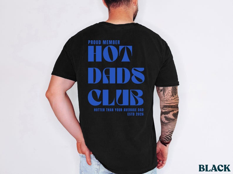 May include: Black t-shirt with the text "PROUD MEMBER HOT DADS CLUB" in blue. The shirt also includes the phrase "HOTTER THAN YOUR AVERAGE DAD ESTD 2026". The shirt is a classic crew neck.