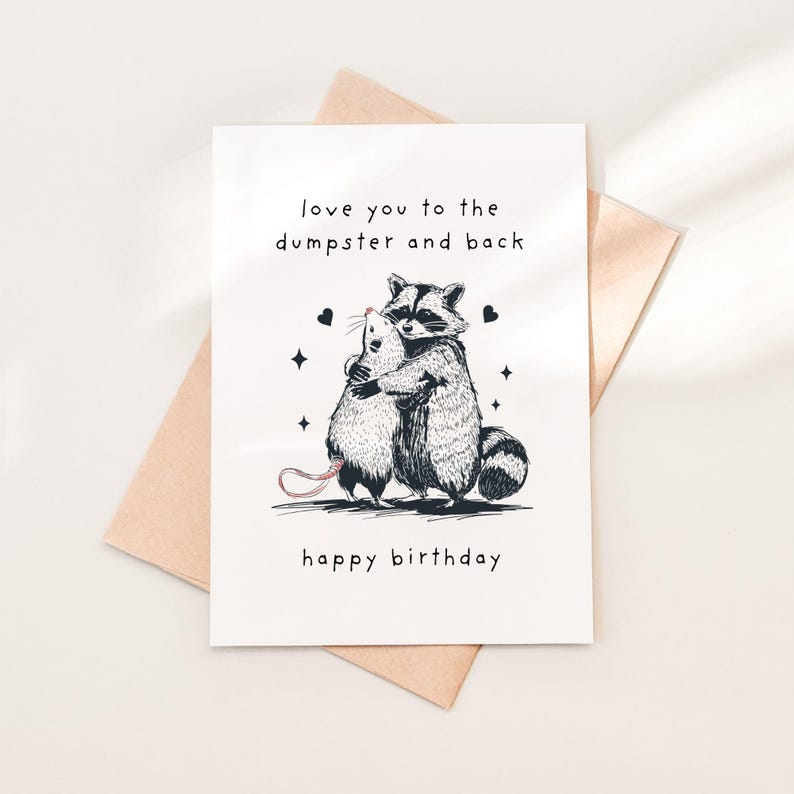 Puede incluir: Una tarjeta blanca con una ilustraci&oacute;n en blanco y negro de un mapache abrazando a una rata. La tarjeta dice "love you to the dumpster and back" y "happy birthday".