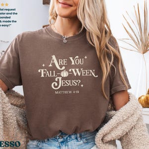 May include: Espresso-colored t-shirt with the text "Are You Fall-Ween Jesus?" in a cream-colored font. The shirt also features the text "Matthew 4:19". The shirt is part of a fall-themed collection.