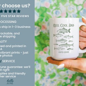 May include: White ceramic mug featuring the text "REEL COOL DAD" and grey fish illustrations. The mug also has "ESTD 2026". The mug is held by a person.