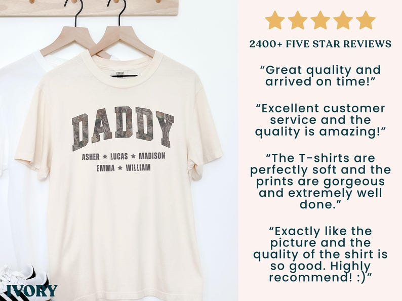 K&ouml;nnte beinhalten: Cremefarbenes T-Shirt mit dem Wort "DADDY" in Camouflage-Schrift. Darunter stehen die Namen Asher, Lucas, Madison, Emma und William. Das T-Shirt h&auml;ngt an einem Holzkleiderb&uuml;gel.