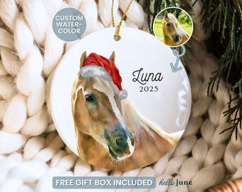 May include: A white ceramic Christmas ornament with a watercolour painting of a horse wearing a Santa hat. The ornament is inscribed with the name "Luna" and the year "2025". It hangs by a gold string. The words "Custom Watercolour" and "Free Gift Box Included" are also visible.