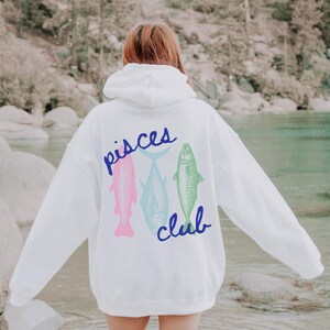 May include: White hoodie with a blue "Pisces Club" graphic featuring three fish in pink, blue, and green.