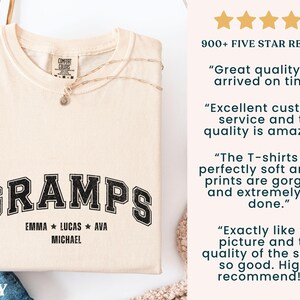 May include: Ivory-colored t-shirt with the word "GRAMPS" in a black, collegiate-style font. Below the word are the names Emma, Lucas, Ava, and Michael. The shirt has a crew neck and short sleeves.