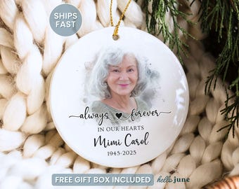 May include: A white ceramic memorial ornament featuring a photo of a woman with gray hair. The ornament includes the text "always forever in our hearts" and the name "Mimi Carol 1945-2025". A gold string is attached for hanging.